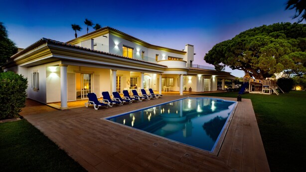 Una casa moderna con piscina, terraza cubierta y césped bien cuidado.