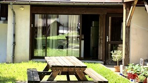 Een houten picknicktafel in een gazon, met een geplaveid pad naar de ingang van een gebouw.