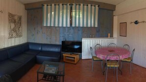 Un saló amb un sofà blau, un armari de fusta, una televisió i una taula de dinar amb cadires.