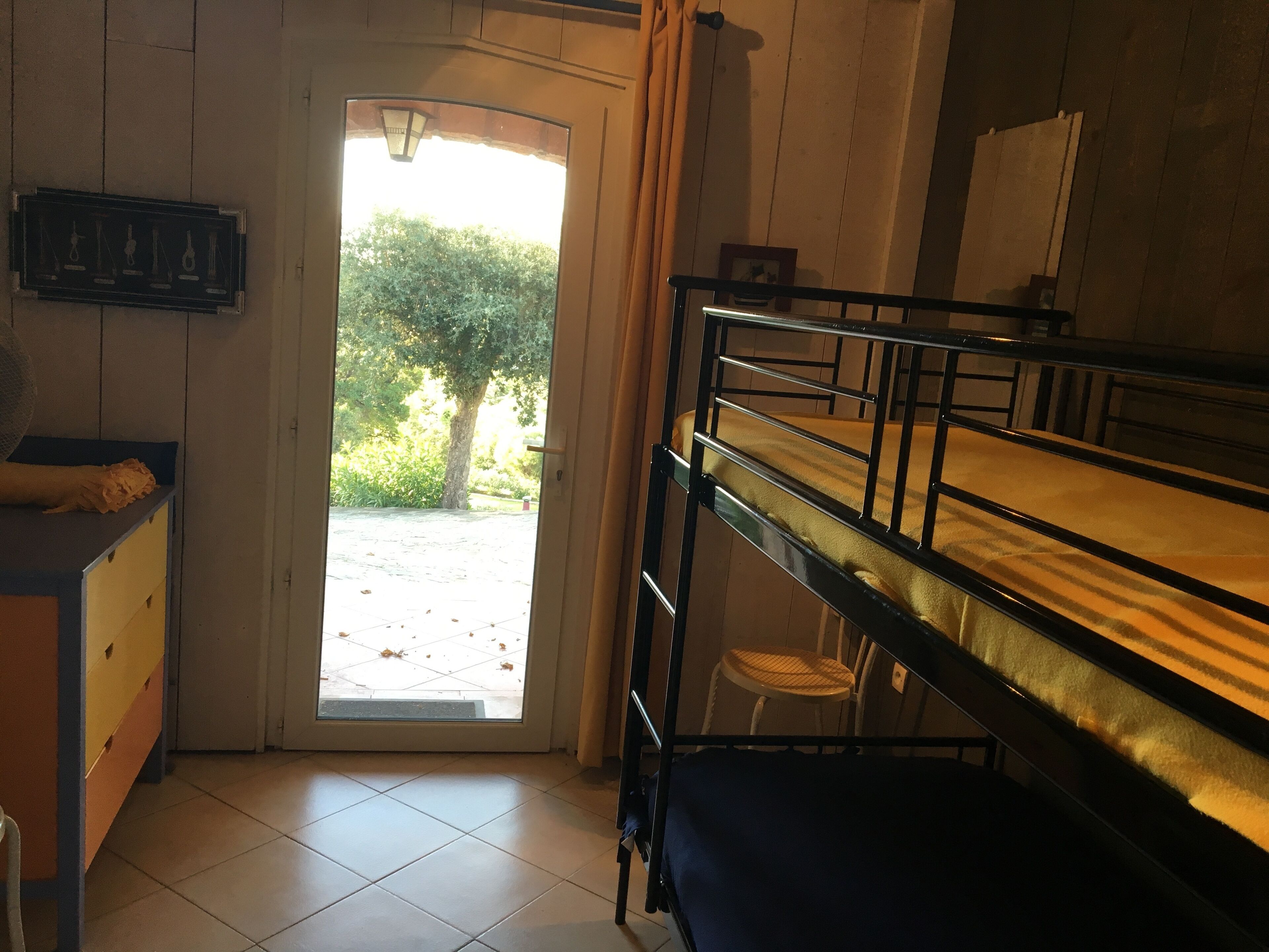 A dormitory room with bunk beds, a desk, and a door leading to a garden.