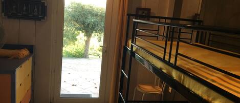 A dormitory room with bunk beds, a desk, and a door leading to a garden.