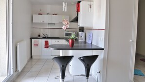 A modern kitchen with white cabinets, a black countertop, and two black bar stools. - Furnished studio, near beach and town center, WIFI  (Annecy)