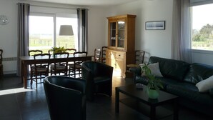 Un salon comprenant un coin repas, un canapé vert, un meuble en bois et une vue par la fenêtre.