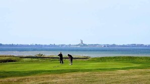 Un parcours de golf offrant une vue sur une étendue d’eau et une tour située au loin.
