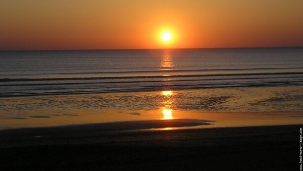 Un coucher de soleil sur une plage, avec une eau calme qui reflète la lumière du soleil.