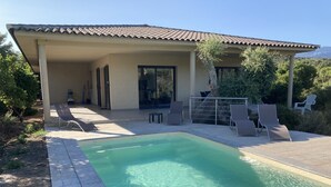 Un área de piscina con sillones de descanso y un porche cubierto.