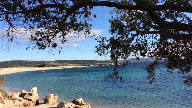 Un paisaje costero con aguas azul cristalino, playa arenosa y afloramientos rocosos.