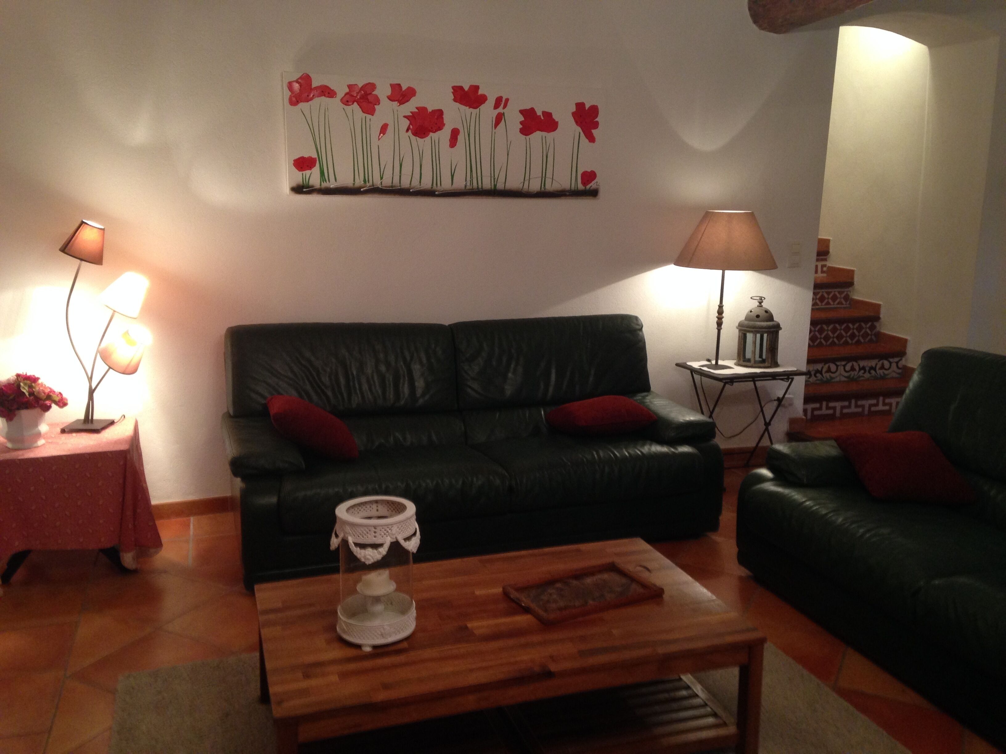 A living room with a black leather sofa, a wooden coffee table, and a wall art piece.