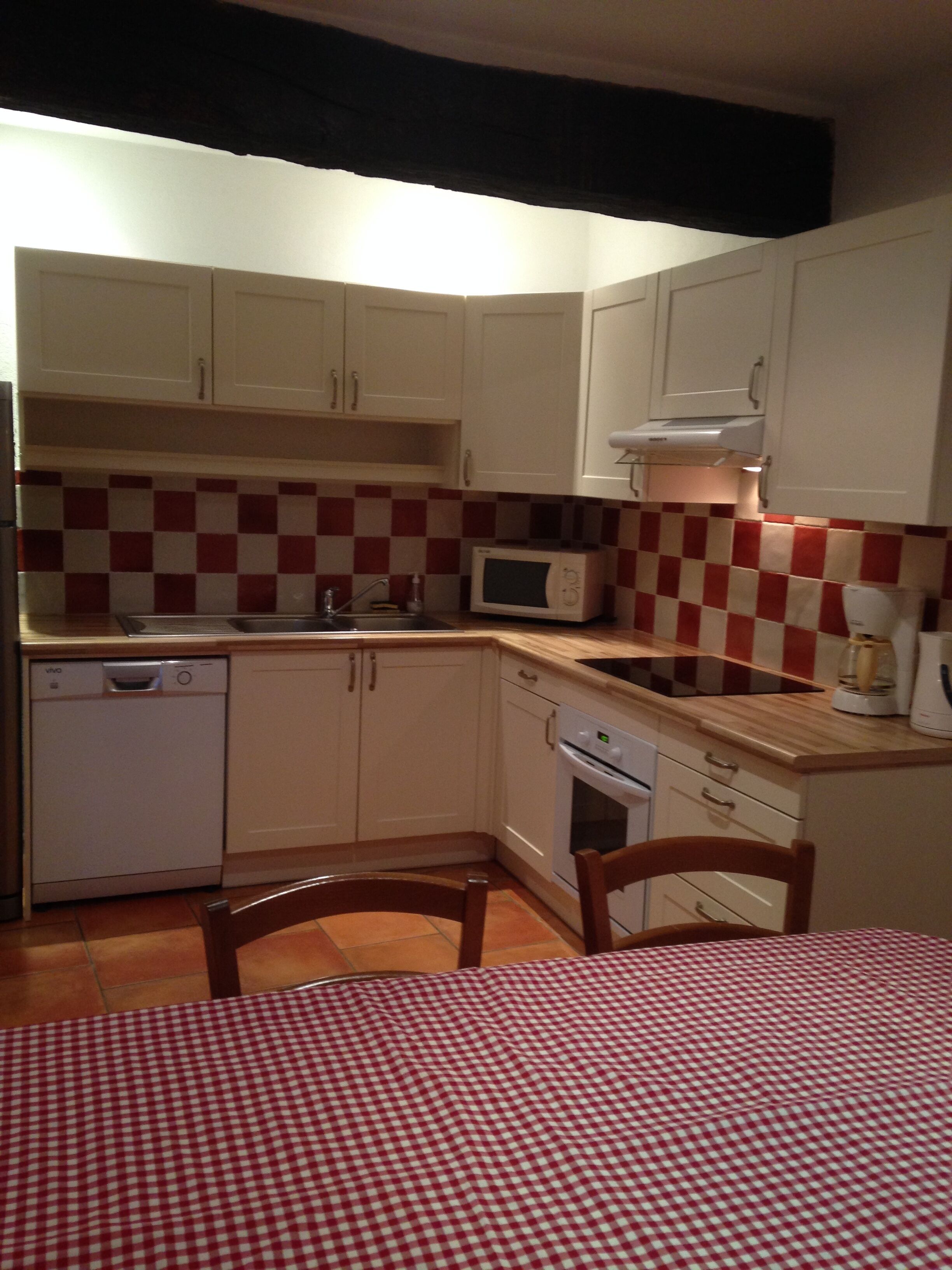 A compact kitchen with white cabinets, a microwave, a dishwasher, and a checkered red and white backsplash.