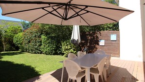 Un patio al aire libre con una mesa y sillas, un gran paraguas y una valla de madera al fondo.