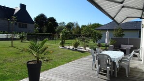Une terrasse en bois avec des meubles d’extérieur, un espace abrité et une pelouse bien entretenue.