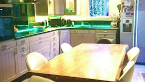 Une cuisine moderne avec une table et des chaises en bois, des plans de travail verts et un luminaire suspendu.