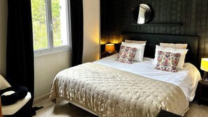 Une chambre à coucher avec un grand lit, deux lampes de chevet, un miroir rond au-dessus du lit et une fenêtre avec des rideaux.