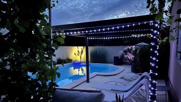 Un jardin avec une piscine, des chaises longues et des guirlandes lumineuses.