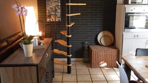 Une cuisine avec une étagère en bois en forme d’échelle, une orchidée en pot, un panier en osier et un coin repas avec une chaise.