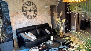 Un salon avec un mur en pierre, un canapé en cuir noir, un tapis en peau de vache et une horloge décorative.