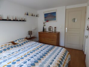 Ett sovrum med en säng, en byrå, hyllor med dekorativa föremål, en tavla och en dörr.