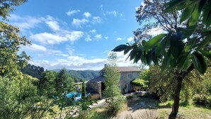 A stone house with a swimming pool, surrounded by lush greenery and mountains in the background. - Gite des Baragnas in the heart of Cévennes nature, air-conditioned, internet, swimming pool (Saint-Jean-Du-Gard)