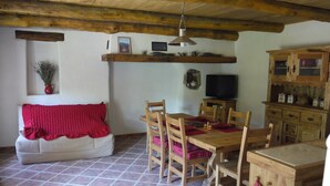 A dining area with a wooden table and chairs, a television, and a cabinet with kitchenware. - Gite des Baragnas in the heart of Cévennes nature, air-conditioned, internet, swimming pool (Saint-Jean-Du-Gard)