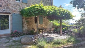 A stone building with a wooden table and chairs under a vine-covered pergola. - Gite des Baragnas in the heart of Cévennes nature, air-conditioned, internet, swimming pool (Saint-Jean-Du-Gard)