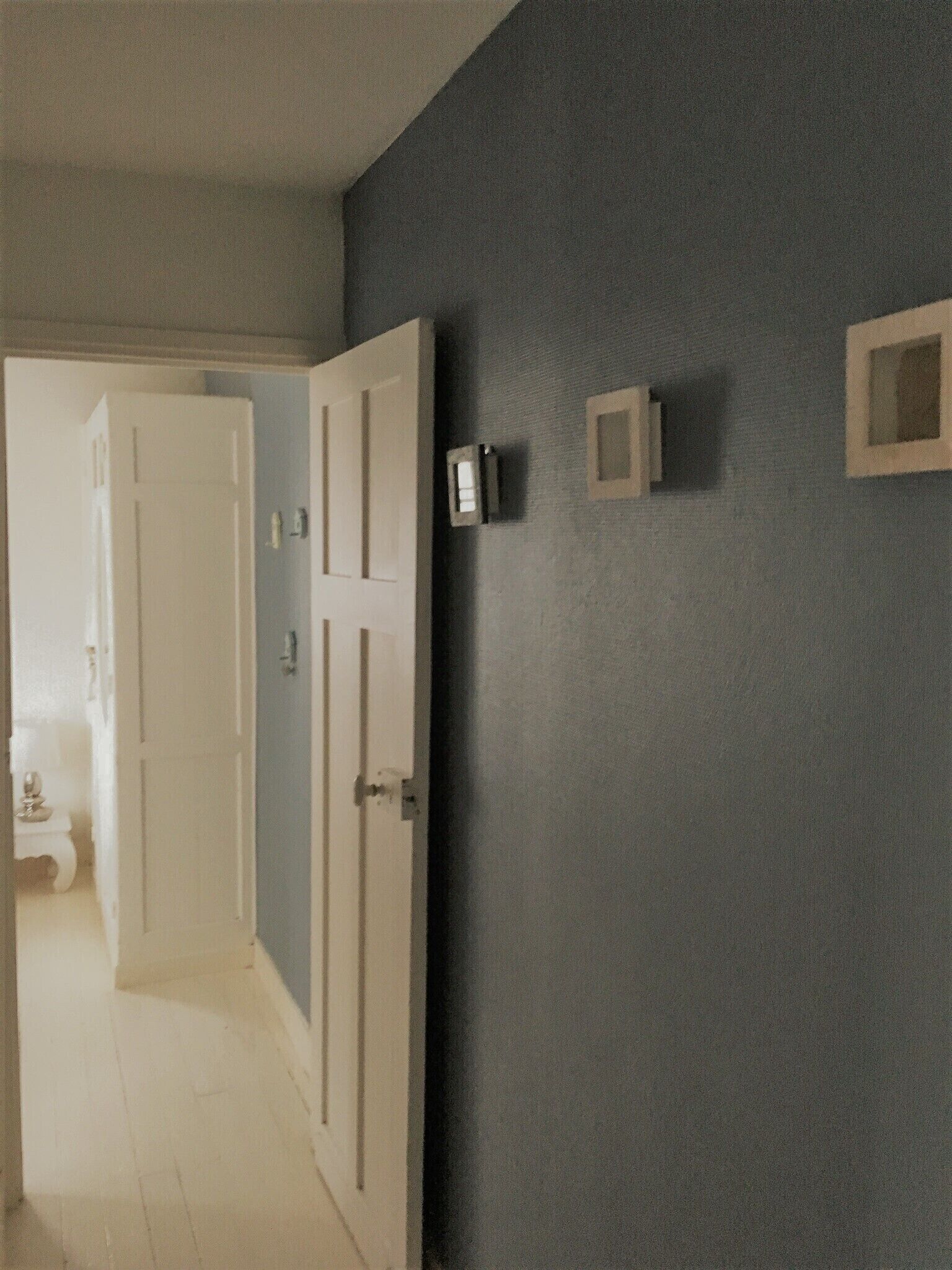 Een gang met een witte deur, een lichtschakelaar en een kleine vierkante lamp aan de muur.