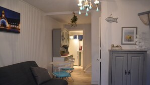 Un salon chaleureux avec un canapé foncé, un coin repas avec une table et des chaises, une cuisine en arrière-plan et un meuble gris orné d’une pancarte d’accueil en forme de poisson.