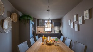 A dining area with a long wooden table, grey upholstered chairs, and a hanging light fixture. - ST REMY DE PROVENCE APARTMENTS AND LOFTS (Saint-Rémy-De-Provence)