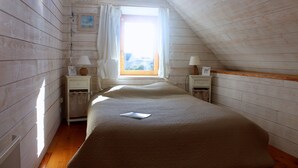 A bedroom with a sloped ceiling, wooden walls, a bed with a white comforter, two bedside tables with lamps, and a window with a view. - Pretty, well-equipped house, close to the sea and fishing port, ideal for children. (Penmarch)