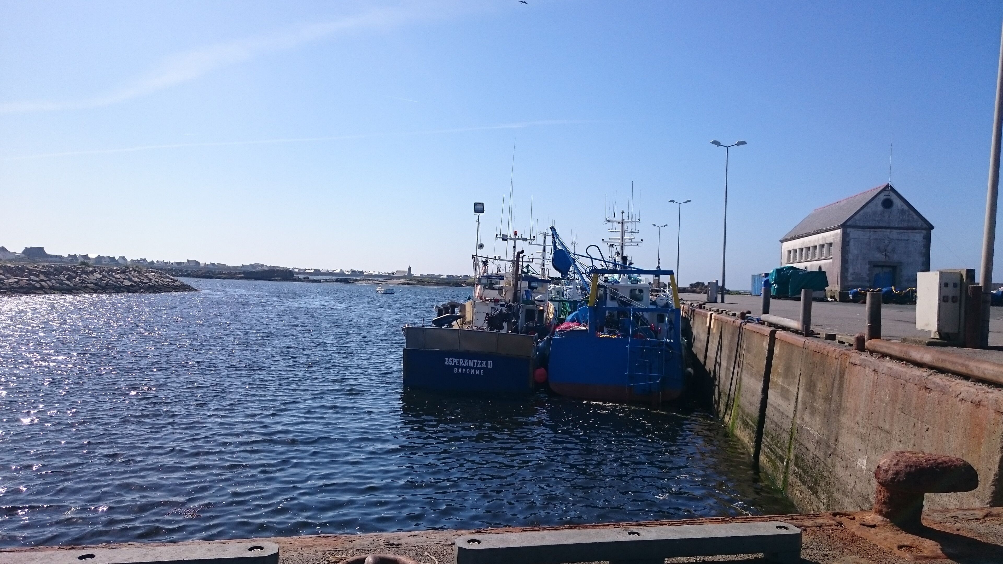En havn med to både ved kaj, en bygning med saddeltag, og en klar himmel.