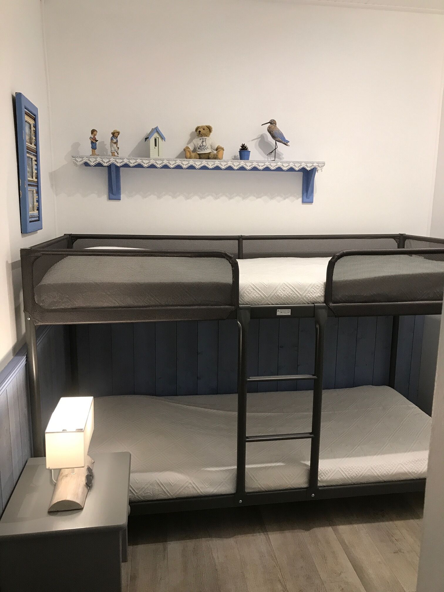 Un lit superposé avec une échelle, une table de chevet avec une lampe et une étagère avec des objets décoratifs.