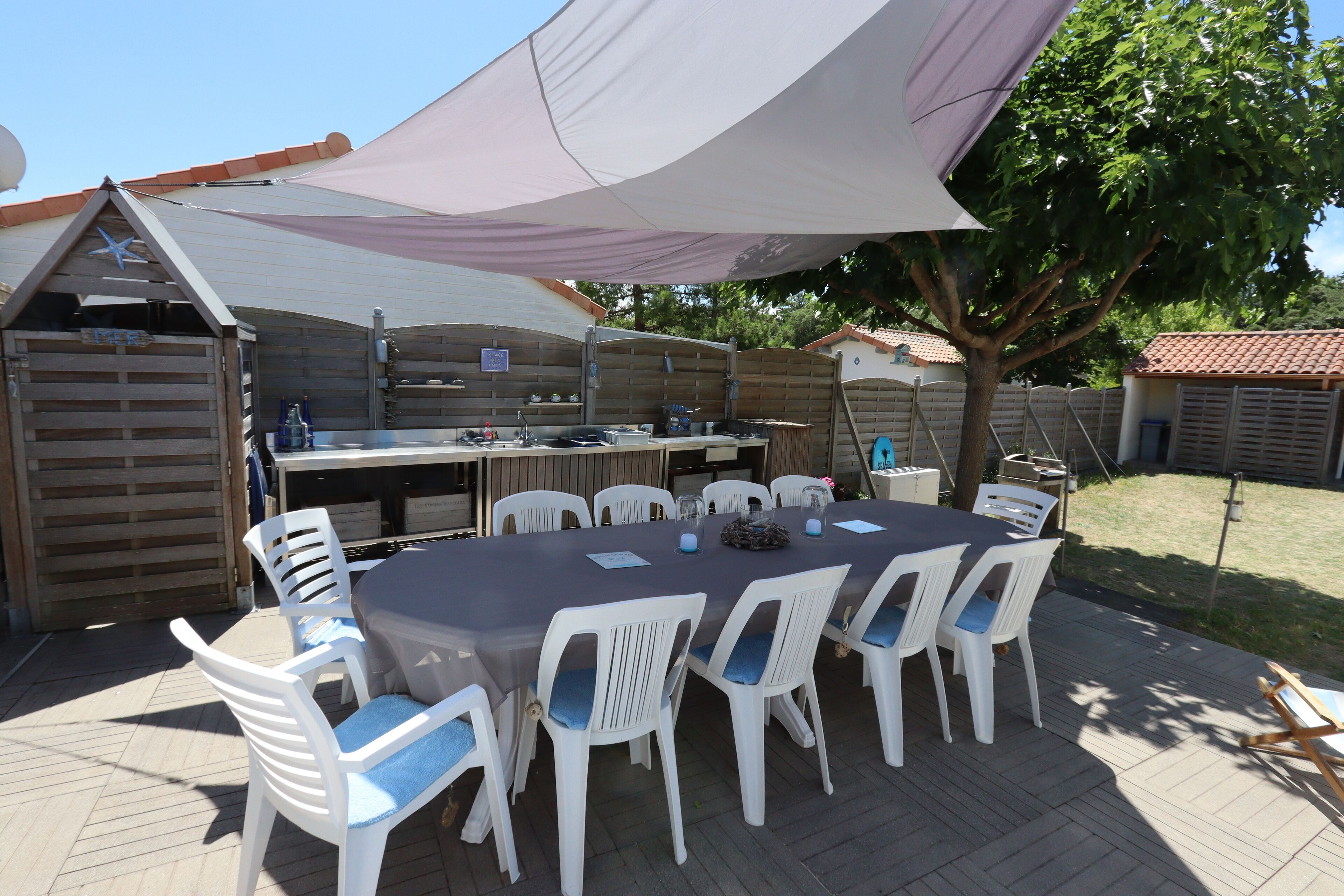 A covered outdoor dining area with a table and chairs, a grill, and a wooden fence.