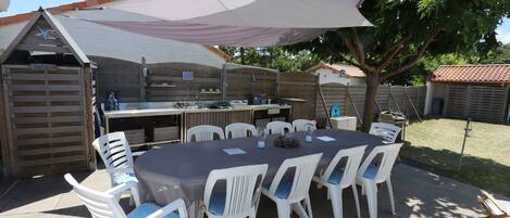 A covered outdoor dining area with a table and chairs, a grill, and a wooden fence.