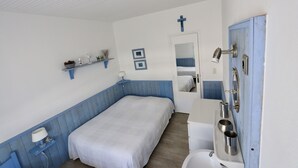 Um quarto com cama, mesinha de cabeceira, prateleira fixada na parede com objetos decorativos, espelho e porta com puxador.