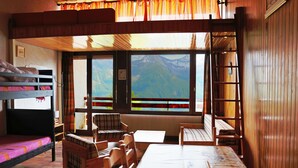 A cozy room with a bunk bed, a wooden table, and a view of mountains through large windows. - Studio for rent located in heart of French Alpes for up to 5 people (Orcières)