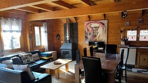 Interior acogedor de una cabaña con piso de madera, un sofá, una mesa de comedor con sillas, una chimenea y un televisor.