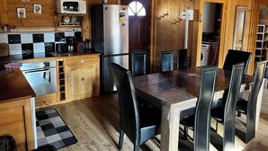 Cocina de cabaña de madera con una mesa de comedor y sillas, un refrigerador, un microondas y una cafetera.