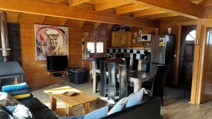 Un interior cálido de cabaña con sala de estar, comedor, cocina y chimenea.