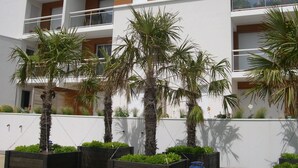 Een modern meerhoogpand met balkons, palmbomen en een witte gevel.