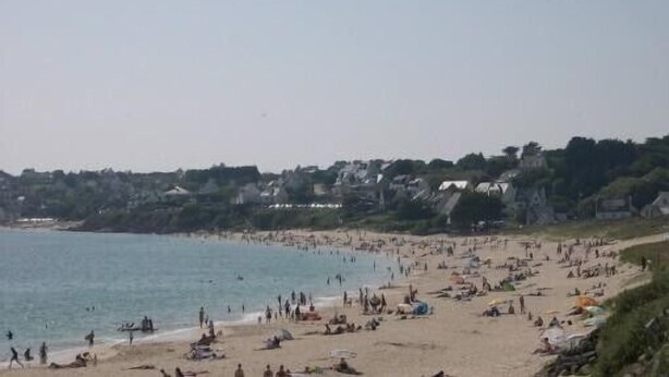 Een druk strand met mensen en parasols, een heldere lucht en gebouwen op de achtergrond.