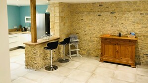 A kitchen with a stone wall, a wooden cabinet, and two black bar stools. - Quiet House 300m Landing Beach 6 Pers (Asnelles)