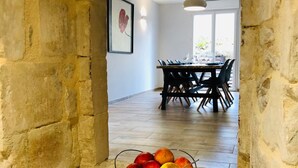 A stone-framed doorway leading to a dining area with a table and chairs, and a fruit bowl on the floor. - Quiet House 300m Landing Beach 6 Pers (Asnelles)