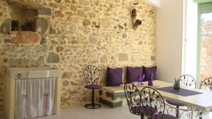 A stone-walled room with a dining table, purple cushions, and metal chairs. - DUPLEX IN OLD MASTER HOUSE SWIMMING POOL, GARDEN, PARKING BEACHES 8 Km away (Pomérols)