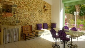 A stone-walled room with a wooden chest, a bench, and a table with purple chairs. - DUPLEX IN OLD MASTER HOUSE SWIMMING POOL, GARDEN, PARKING BEACHES 8 Km away (Pomérols)