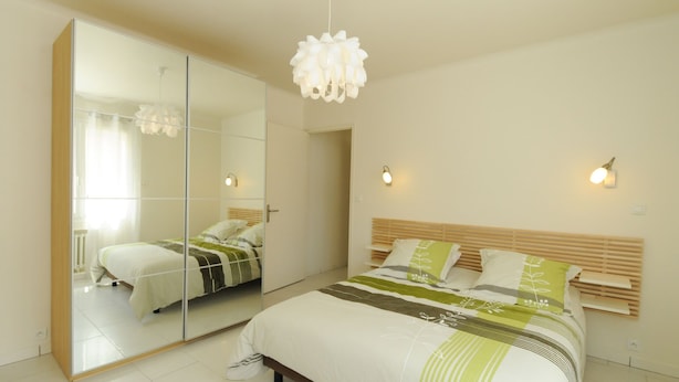 A bedroom with a bed, a large mirror, and two wall-mounted lights. - Gîte Boucle de Meuse 150 m voie verte, 3 km Sedan. 3 bicycles, indoor table tennis. (Glaire)