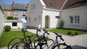 A residential area with a white house, a gravel driveway, and bicycles parked in the foreground. - Gîte Boucle de Meuse 150 m voie verte, 3 km Sedan. 3 bicycles, indoor table tennis. (Glaire)