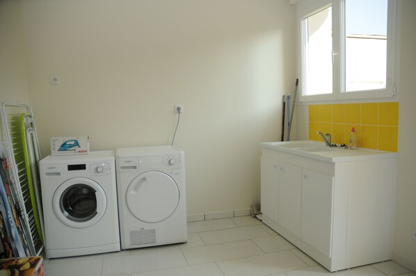 A laundry area with two white washing machines, a white sink, and a window with yellow tiles.