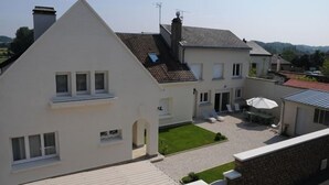 A two-story house with a sloped roof, a small front yard, and a patio area with outdoor furniture. - Gîte Boucle de Meuse 150 m voie verte, 3 km Sedan. 3 bicycles, indoor table tennis. (Glaire)