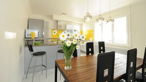 A modern kitchen with a dining area, featuring a wooden table, chairs, and a vase of flowers. - Gîte Boucle de Meuse 150 m voie verte, 3 km Sedan. 3 bicycles, indoor table tennis. (Glaire)