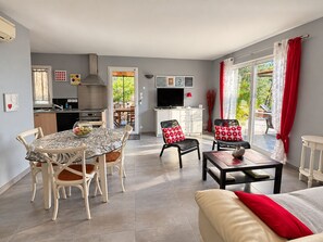 Una cocina moderna con comedor, una sala de estar con sofá y sillones, y un amplio ventanal corredera al exterior.