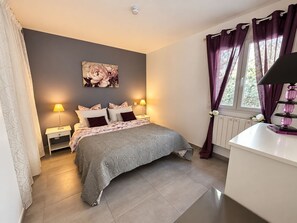 A bedroom with a bed, nightstands, a lamp, a radiator, and a window with curtains.